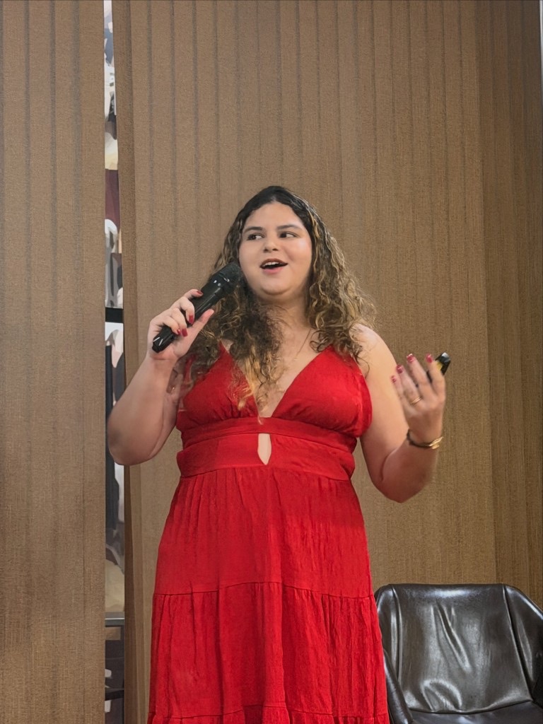 Rebeca Sousa on stage at MMMT 2026, holding a mic and clicker during her talk.